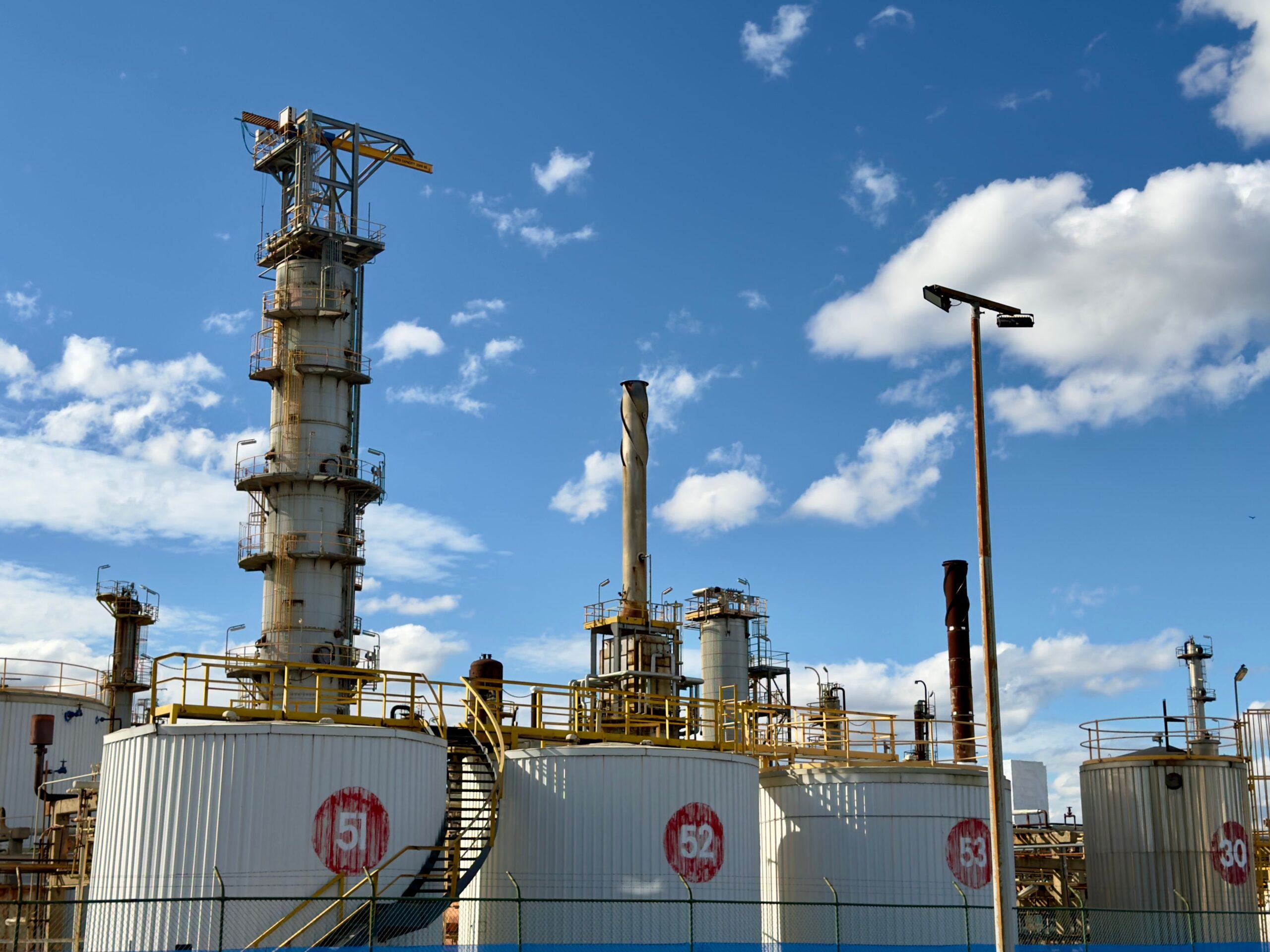 Industrial refinery with storage tanks and towers under a clear blue sky in Altona North, Victoria, Australia.